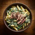 Creamy spinach steak penne pasta with sliced steak in a bowl